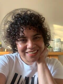 Associate Brunhild Abrahams has black curly hair and is wearing a white and black t-shirt