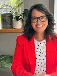 Senior Associate Mish Seabrook has long dark hair and is wearing black glasses, a white top with black dots under a red jacket