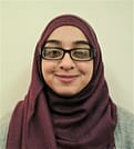 Associate Sheereen Siddat is wearing black glasses and a purple headscarf