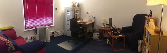 counselling and psychotherapy room: red chair, navy chair, office desk and table, book case, filing cabinet